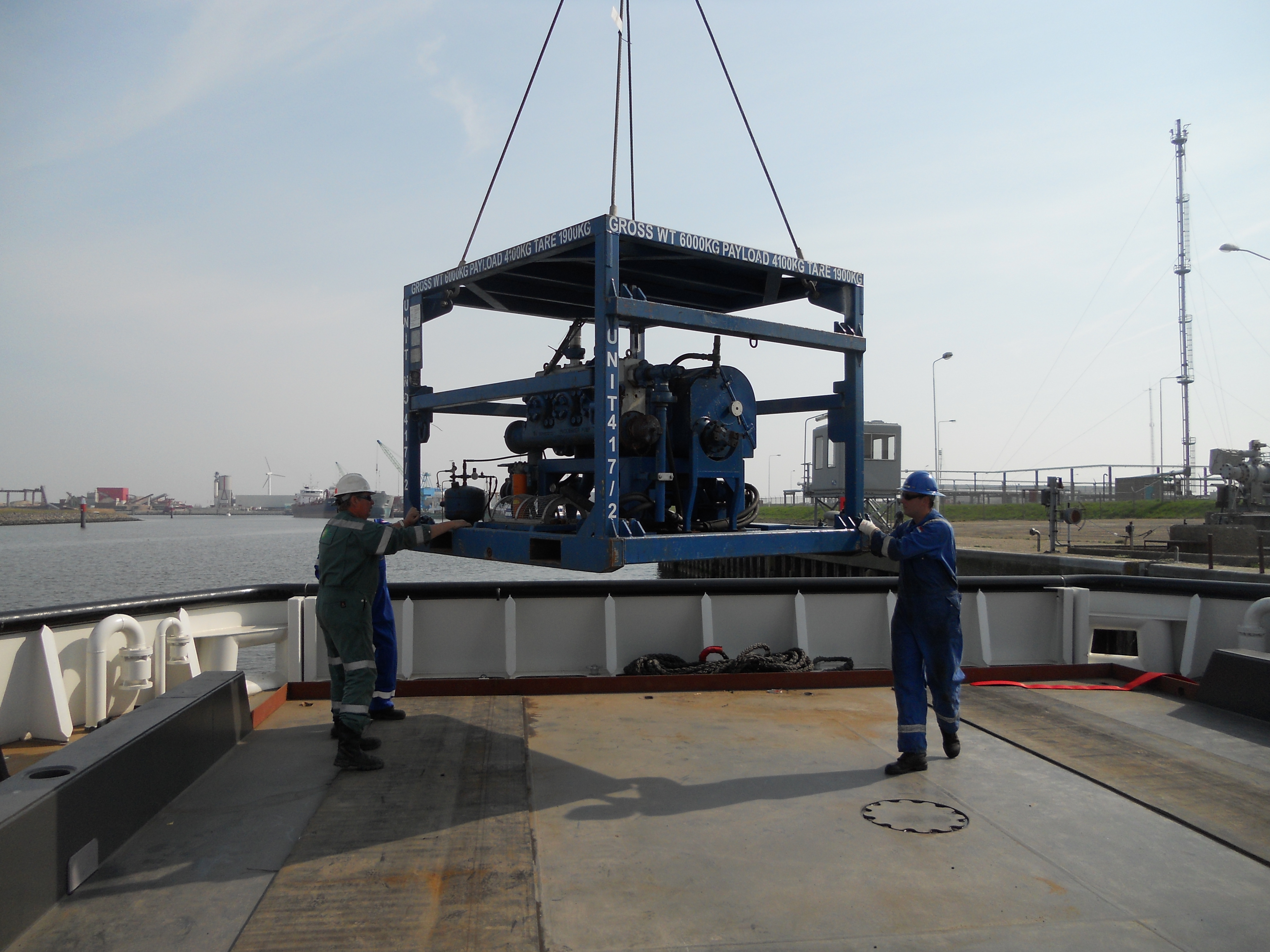 Workers guiding the delivery of heavy industrial equipment onto a vessel, for offshore or on-site operations.