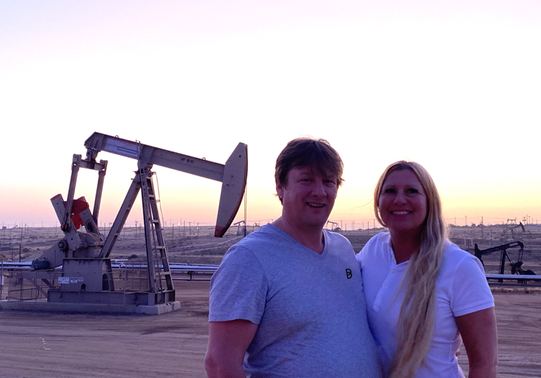 Rod Gibbons and Willow Gibbons, co-founders of Ballycatter, standing in front of an oil pumpjack at sunset.